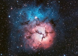 Black background with stars dotting it, in the center of the image is a nebula; it is a pink circle with a blue ring around it